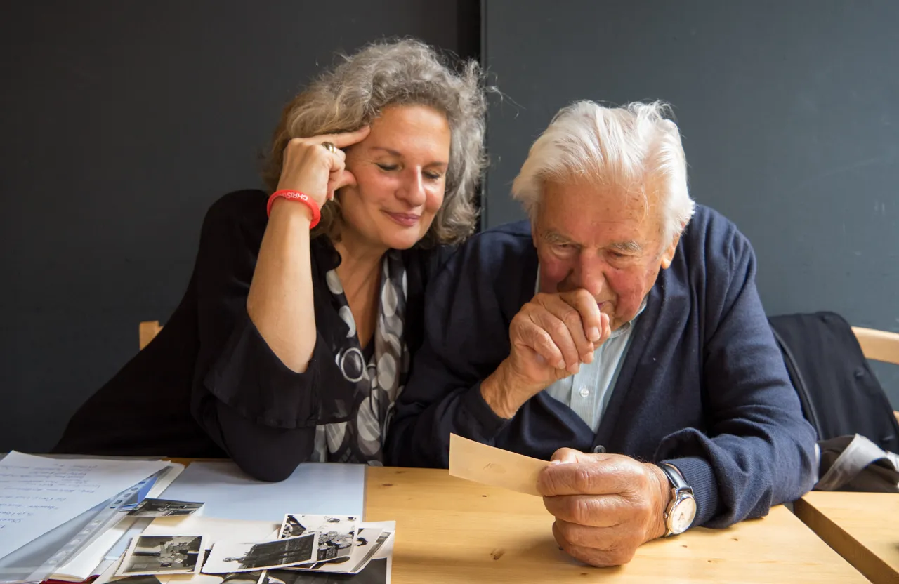 Ulrike Wünnemann und ein älterer Herr beugen sich gemeinsam über alte Fotografien.